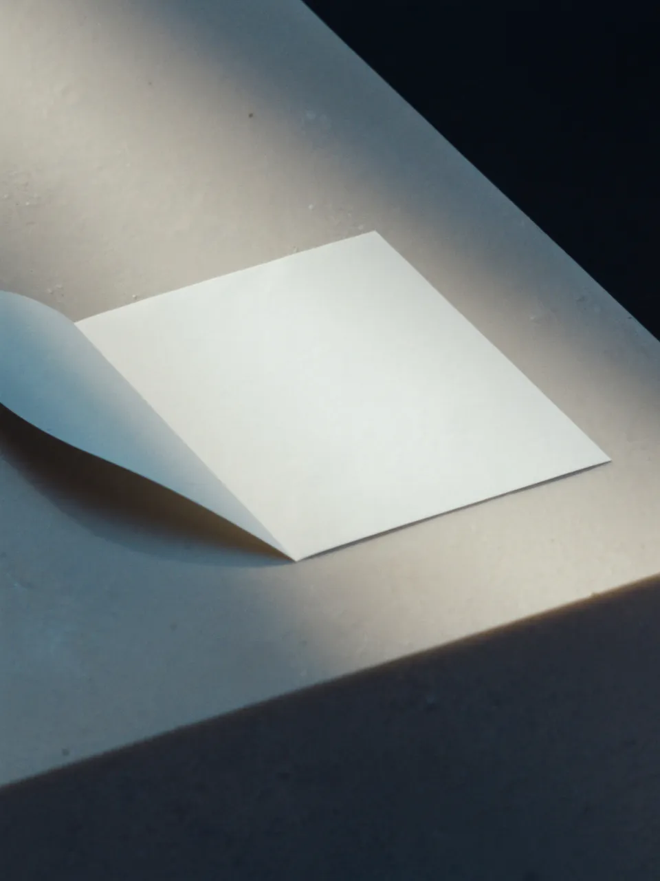 A folded, blank quote on a pale stone slab in hard morning light.