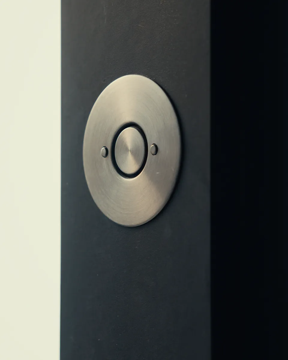 A round brushed steel doorbell set in an anthracite aluminium panel.