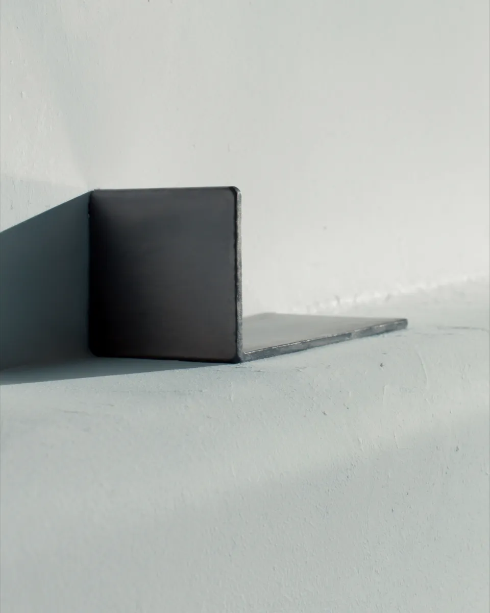 A steel square against a smooth bone-white plaster wall.